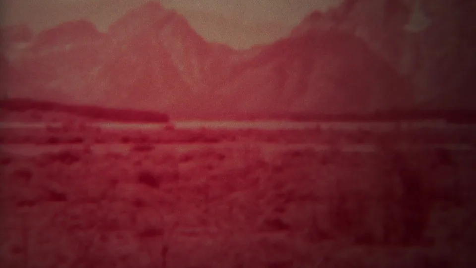 Blurred red-tinted 8mm view of distant rugged peaks beyond a flat foreground in the Yellowstone, Wyoming clip.