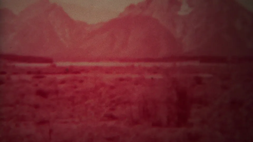 Grainy 1967 8mm frame of a red-tinted mountain range and scrubby open plain in the Yellowstone, Wyoming area.