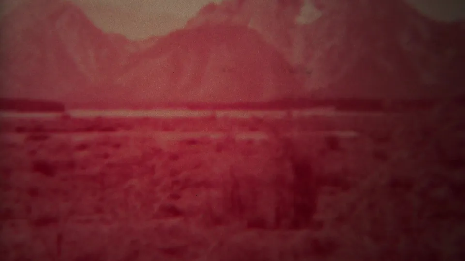 1967 8mm Yellowstone, Wyoming footage showing a red-faded plain, low vegetation, and a hazy mountain range in the distance.