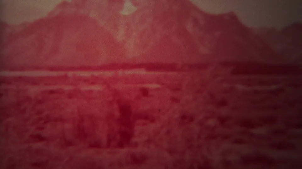A soft 1967 8mm frame from Yellowstone, Wyoming showing low brush across an open plain beneath a hazy mountain backdrop.