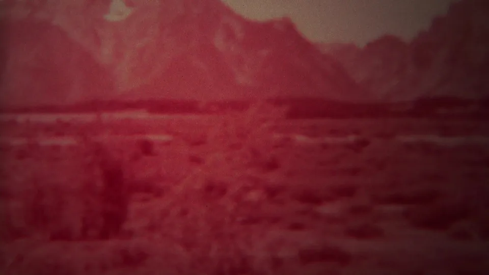 1967 Yellowstone, Wyoming 8mm frame showing a red-tinted open valley, low shrubs, scattered trees, and rugged mountains in soft focus.