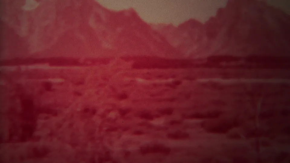 1967 Yellowstone, Wyoming 8mm frame with red-tinted brushland, dark tree forms, a distant mountain range, and hazy sky.