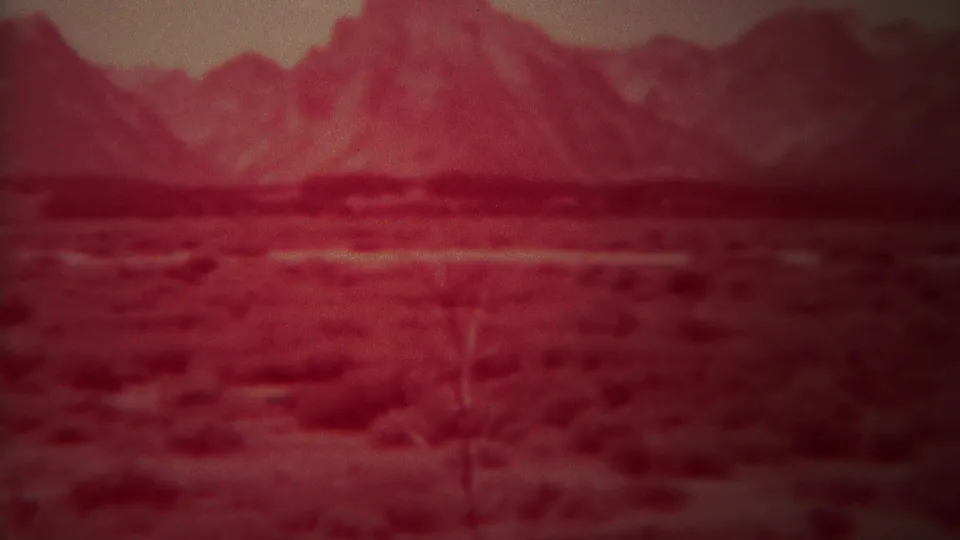 1967 8mm home-movie frame from Yellowstone, Wyoming, showing reddish shrubland stretching toward a soft distant mountain range.