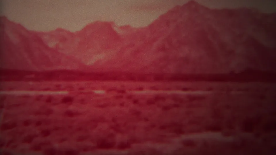 Red-tinted 8mm frame from Yellowstone, Wyoming, showing open shrubland and a distant mountain range with no visible people or structures.