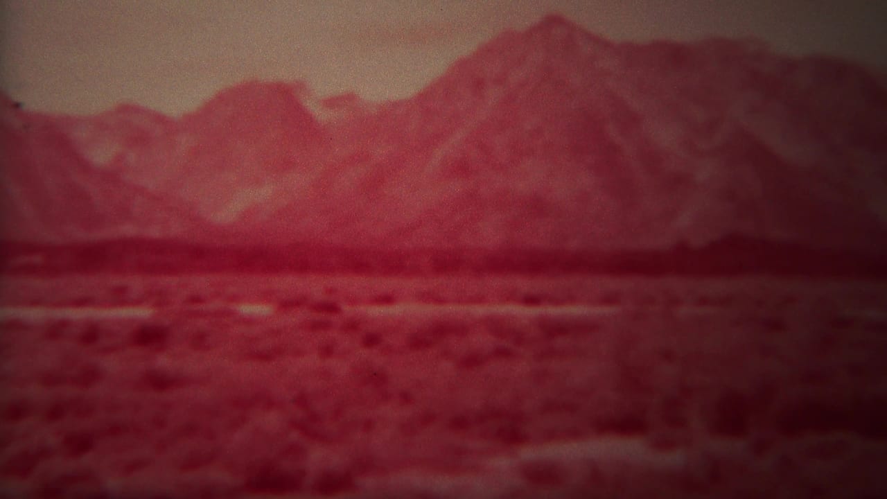 1967 Yellowstone home-movie frame showing distant mountains across open land or water with a reddish film cast and soft focus.