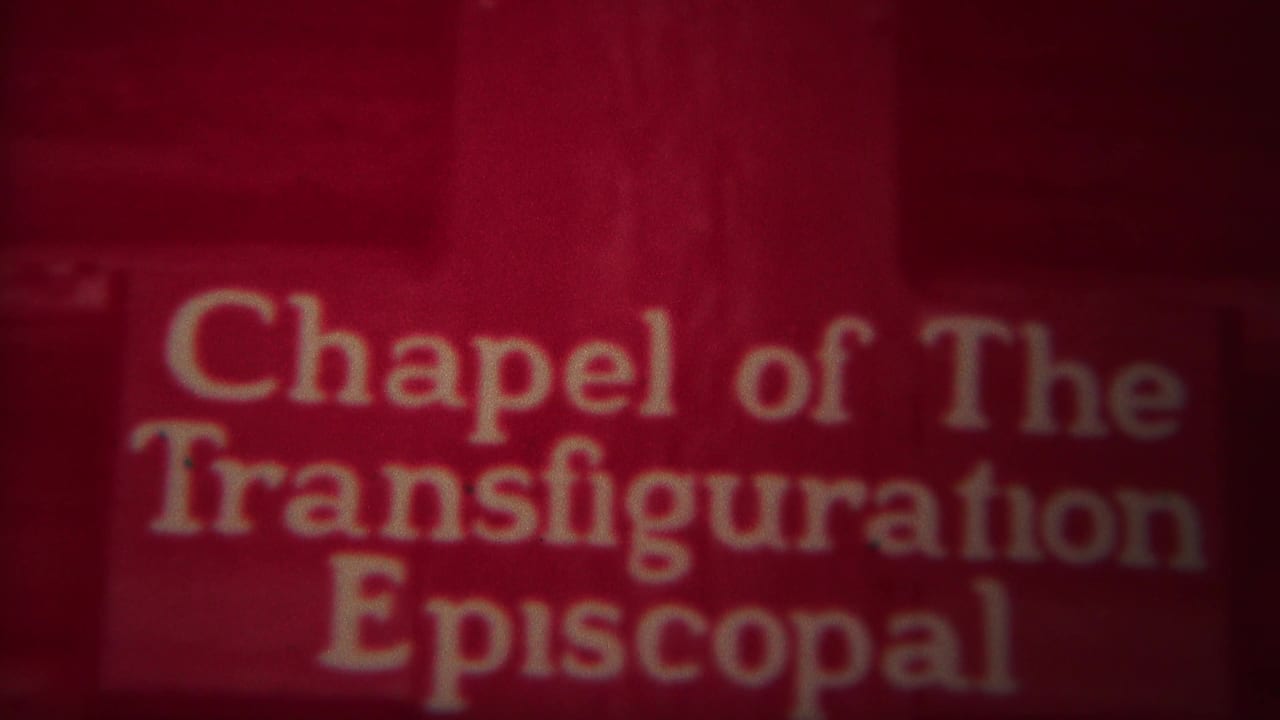 Red-tinted Chapel of the Transfiguration Episcopal sign above a mountain view with a cross.