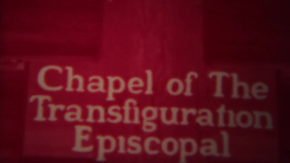 1967 8mm frame showing the Chapel of the Transfiguration Episcopal sign and a mountain scene with a dark cross below.