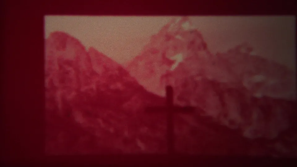 Visitor-shot 1967 8mm view of a cross set against mountains beneath the Chapel of the Transfiguration Episcopal sign.