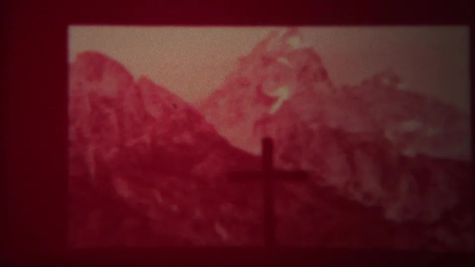 1967 8mm frame from Wyoming showing chapel signage above a cross and mountain landscape, with heavy red tint and grain.