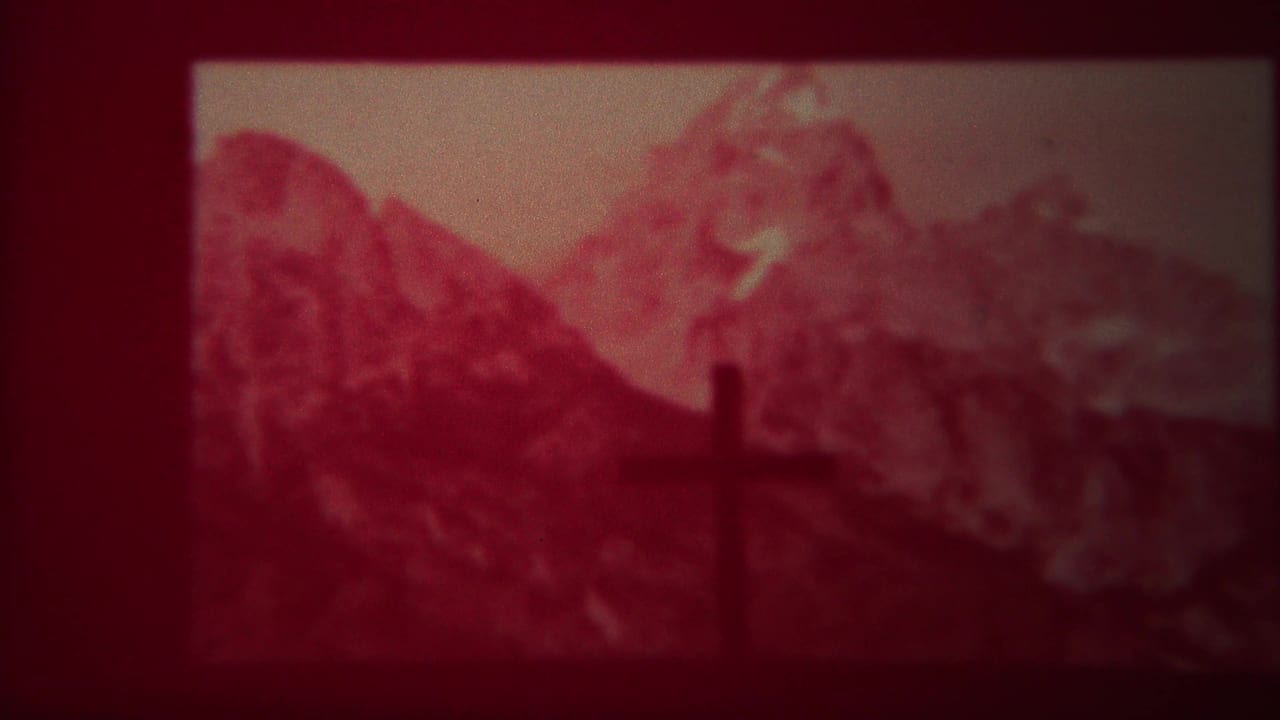 Dark cross-shaped silhouette before red-tinted snow-capped mountains.