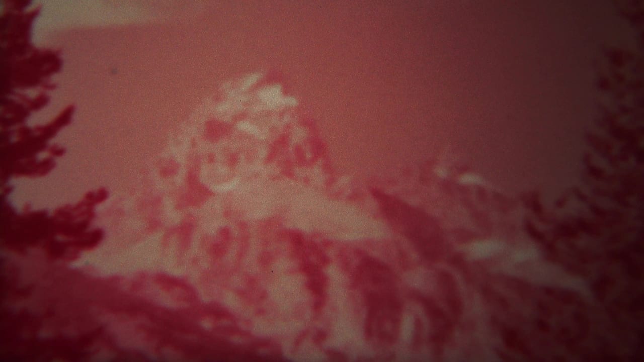 Red-tinted 1967 Yellowstone frame with a pale mountain peak, dark tree silhouettes, and soft 8mm grain.