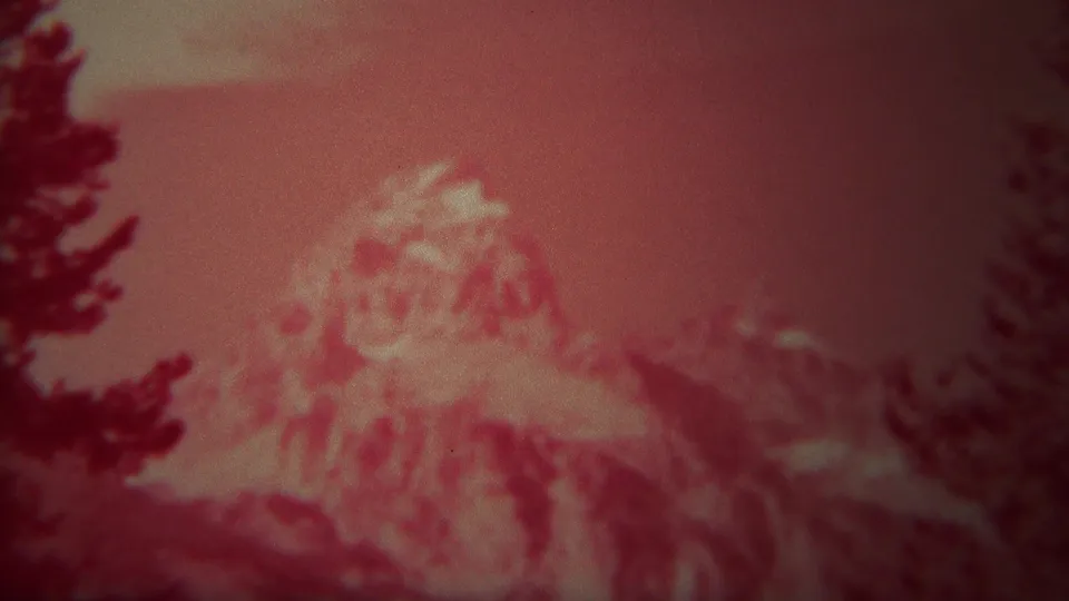 Late frame from the 1967 Yellowstone clip with a red-tinted mountain peak and evergreen silhouettes in soft focus.