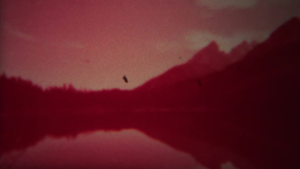 Red-tinted mountain ridge reflected in a still lake with hazy sky.