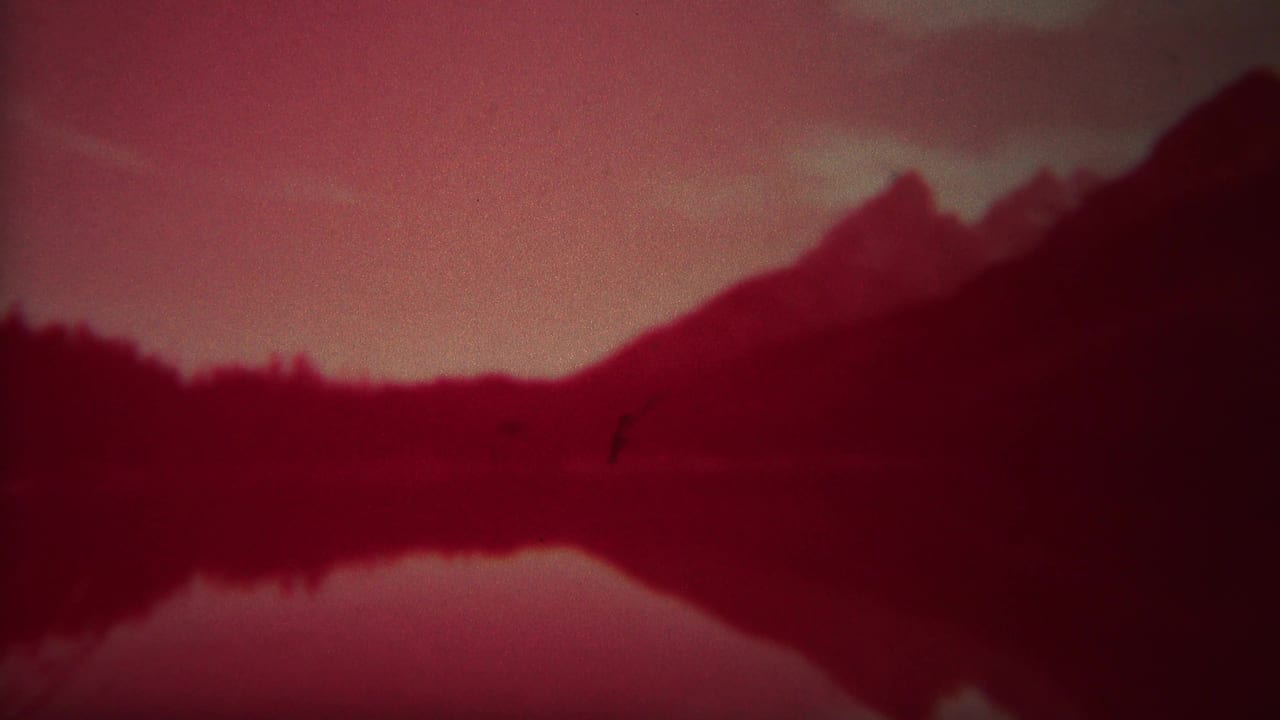 Yellowstone home-movie frame with silhouetted mountains, a low forest edge, and their reflection under a faded red cast.