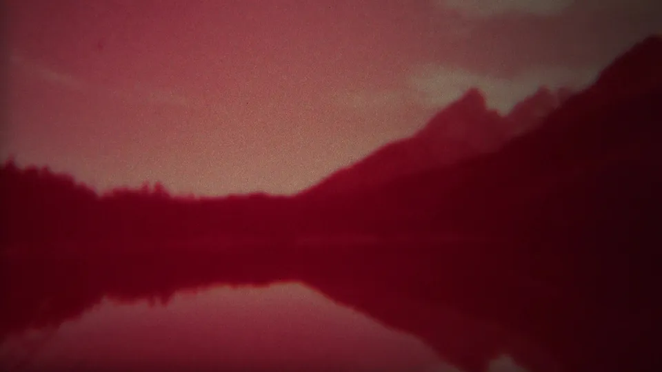 1967 Yellowstone 8mm frame showing a softened mountain slope and dark tree line reflected in still water.