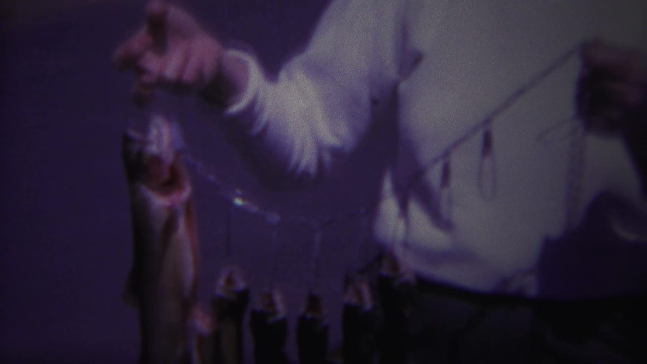 1967 Yellowstone home-movie frame showing a man in a white shirt raising a stringer with a large fish visible against a dark background.
