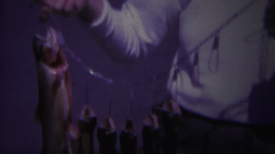 1967 Yellowstone frame with a large fish hanging from a stringer as a man in a white shirt stands partly cropped behind it.