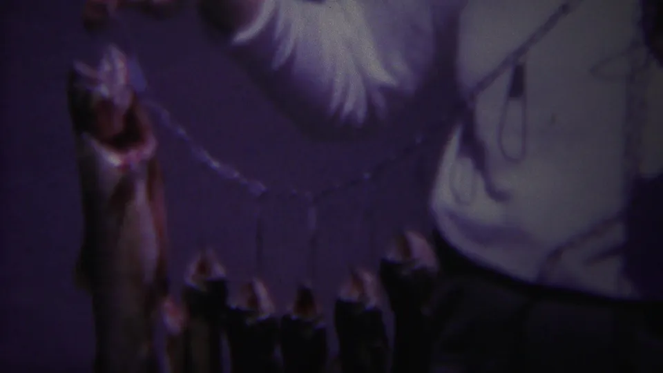 1967 Yellowstone home-movie frame showing multiple fish on a stringer held up by a man in a white shirt, with soft focus and dim exposure.