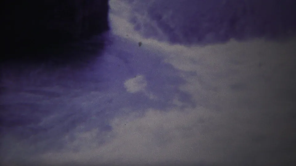 1967 Yellowstone home-movie frame showing blurred rushing water near a dark tree trunk and pale shoreline or bank.