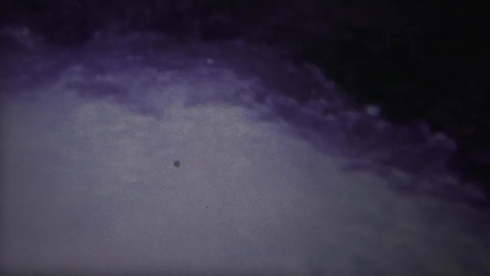 1967 8mm frame from Yellowstone, Wyoming showing pale churning water under a dark purple-blue shadowed bank or outflow edge.