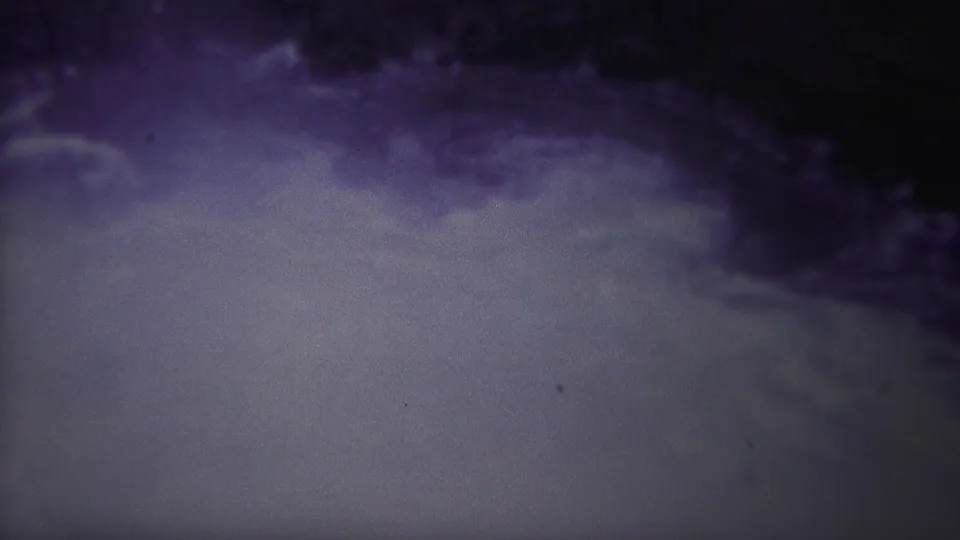 1967 Yellowstone home-movie frame showing agitated river water below a dark bank or rock edge, with heavy grain and purple-gray color shift.
