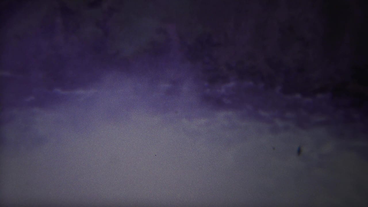 1967 Yellowstone home-movie frame showing a dark, purple-blue natural scene with a pale water or mist area and shadowed terrain.