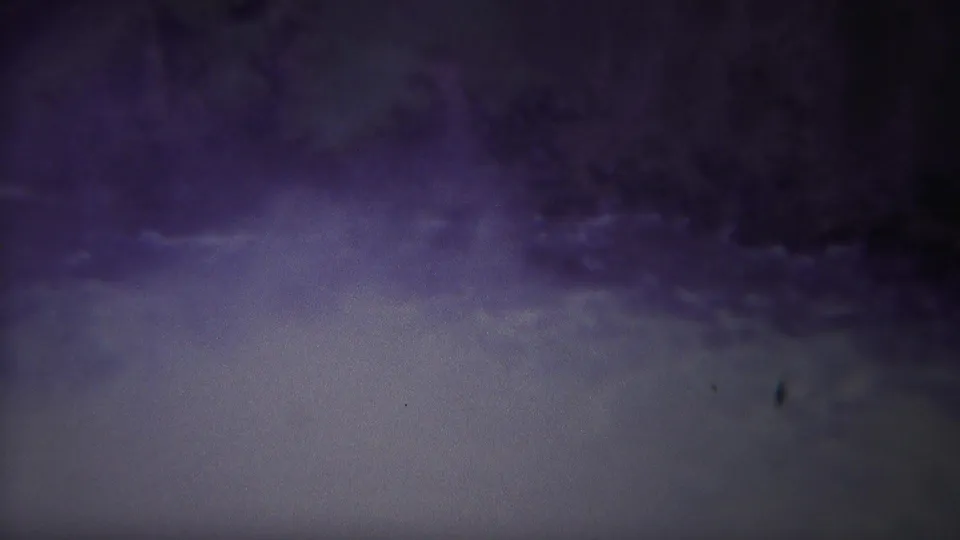 1967 Yellowstone home-movie frame showing a dark, purple-blue natural scene with a pale water or mist area and shadowed terrain.