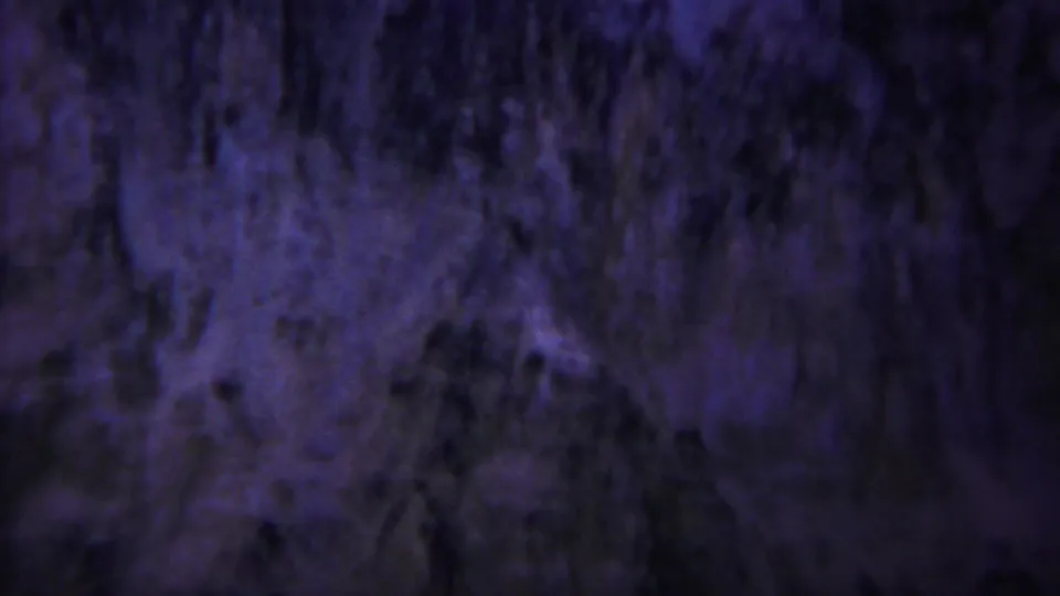Vintage 8mm Yellowstone frame showing blurred purple-blue terrain or rock texture with dark vertical forms and visible grain.