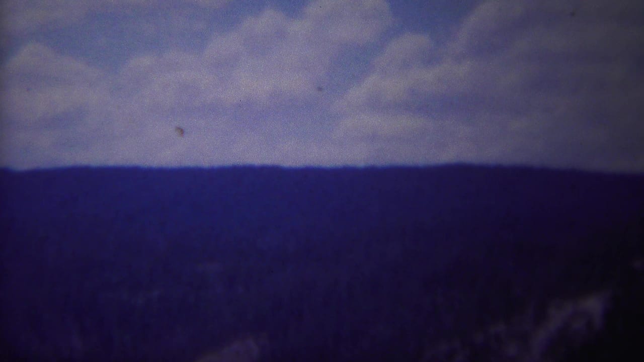 Distant mountain ridge under a cloudy sky with dark forest below.