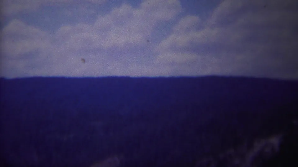 1967 Yellowstone view of a distant ridge line, cloudy sky, and dark pine-covered slopes in soft 8mm color.