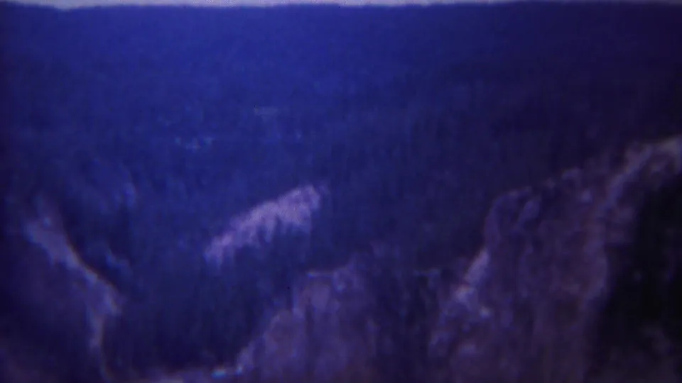 1967 Yellowstone home-movie view of a blue-tinted canyon landscape with forested slopes and pale highlights below.