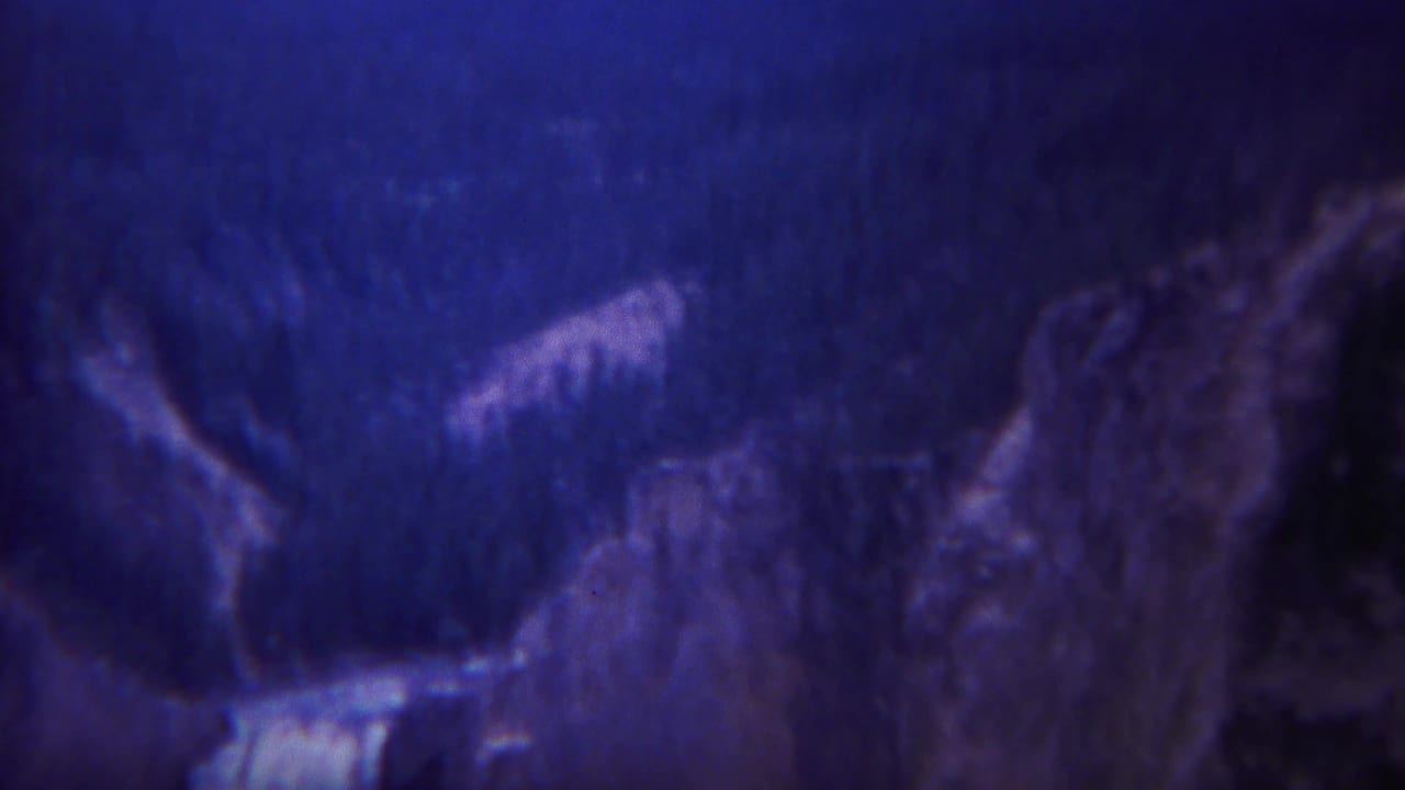 Purple-blue 8mm frame of a waterfall dropping between dark mountain cliffs.