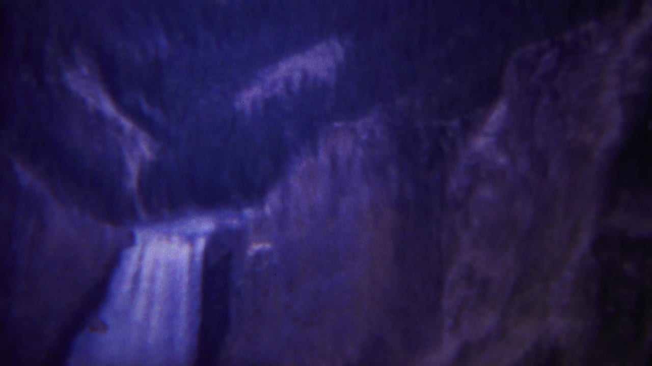 1967 Yellowstone 8mm view of a bright waterfall against dark rock, with forested slopes partly visible.