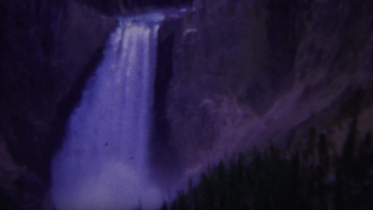 Waterfall centered between rocky slopes and dark forest.