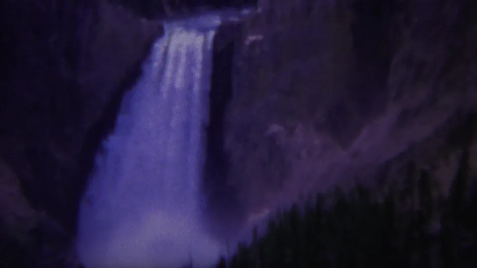 Closer 1967 Yellowstone frame of the waterfall dropping beside a cliff face, with mist or spray collecting near the base.