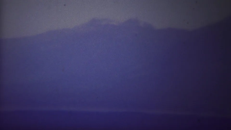 Blue-gray 8mm frame of a hazy mountain ridge and valley, consistent with the 1967 Wyoming travel footage.