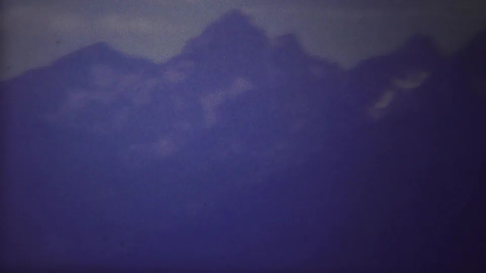 1967 Yellowstone home-movie frame with jagged mountain peaks, mist, and small light patches on the slopes.