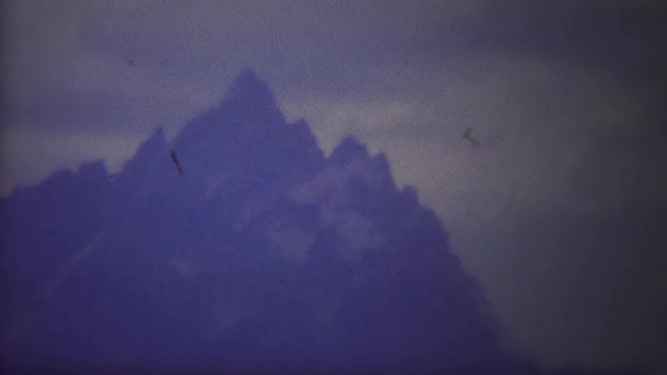 1967 Yellowstone 8mm frame showing a pointed mountain peak and adjacent ridge beneath a gray, overcast sky.
