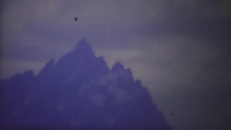 1967 Yellowstone 8mm frame with a central mountain peak, adjoining ridge, and heavy cloud cover in cool archival color.