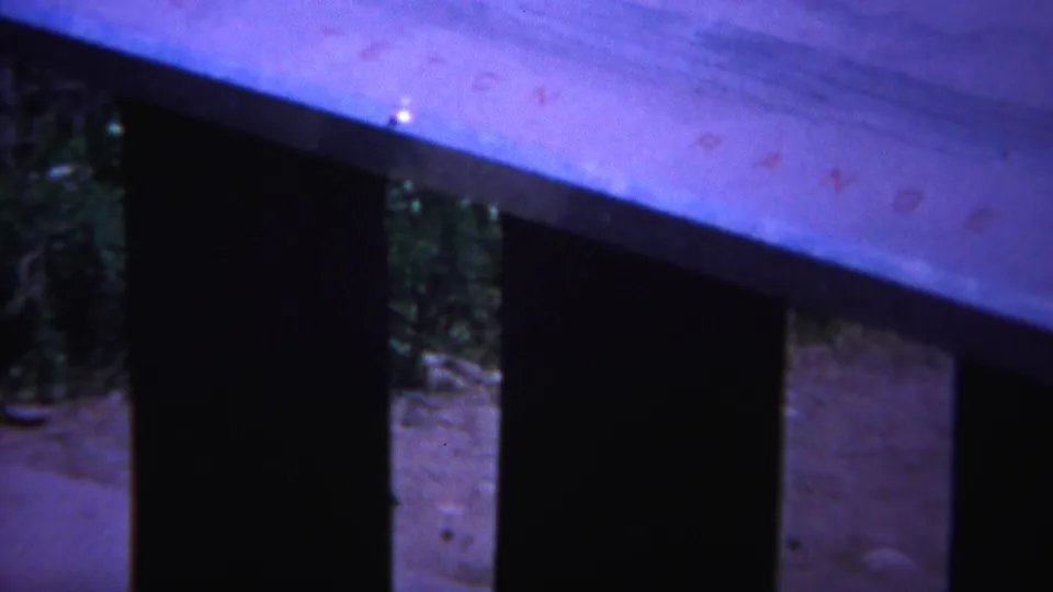 1967 Yellowstone home-movie frame with angled pale wood, dark slats, and a small area of ground or greenery beyond.