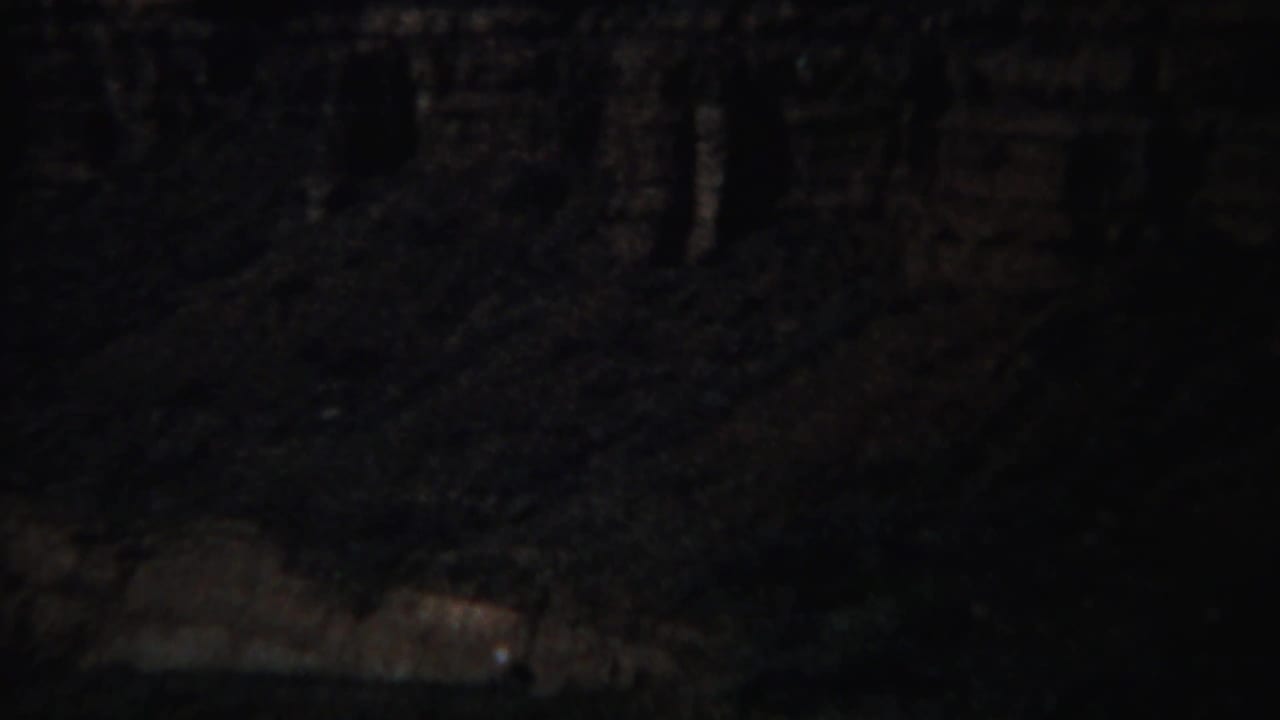 Dark canyon wall with layered rock and shadowed slopes.