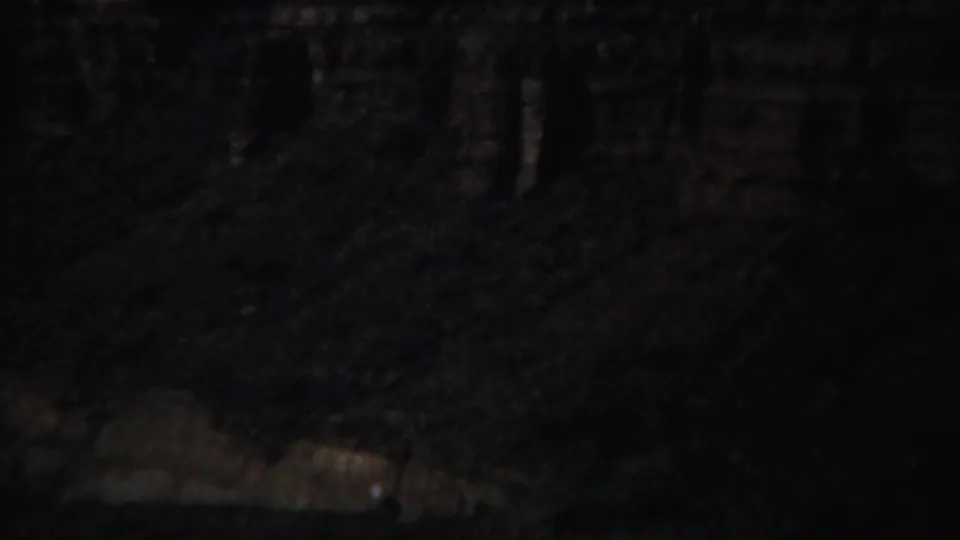 1967 Yellowstone home-movie frame showing a dark canyon wall, pale layered rock, and deep shadow across rugged terrain.