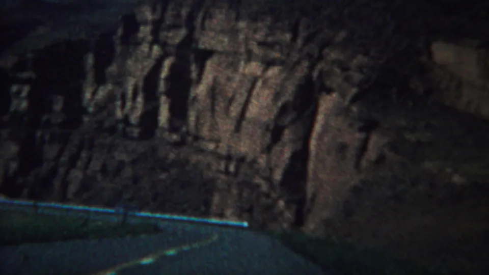 A 1967 Yellowstone roadside view frames steep, shadowed rock formations above a paved mountain road.