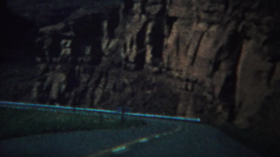 Vintage 8mm Yellowstone frame with a guardrail and road foreground below a dark, textured cliff face.