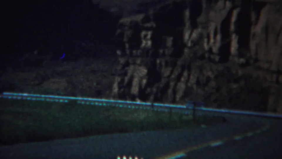 1967 Yellowstone-area 8mm frame showing a dark road, pale guardrail, and rugged canyon wall in deep shadow.