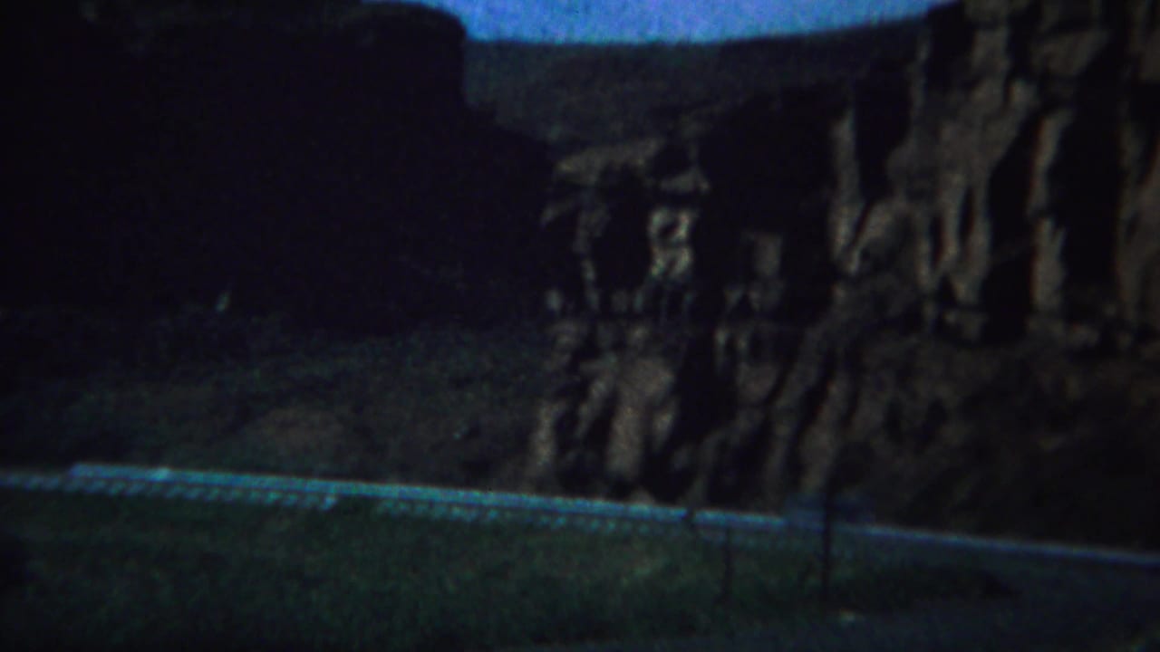 Dark canyon roadway with guardrail and tall rock walls on both sides.