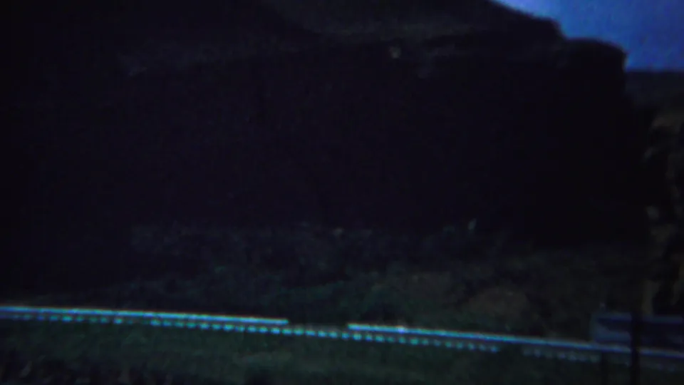 1967 Yellowstone-area 8mm frame showing a dark roadside view with shadowed hills or rock forms and a bright road edge.