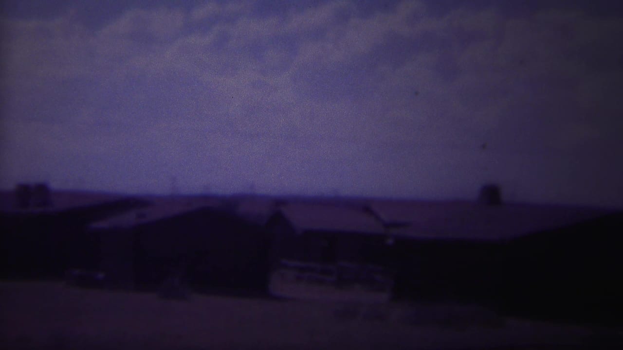 1967 8mm frame from Yellowstone, Wyoming showing dark low buildings under a heavy purple-blue sky.