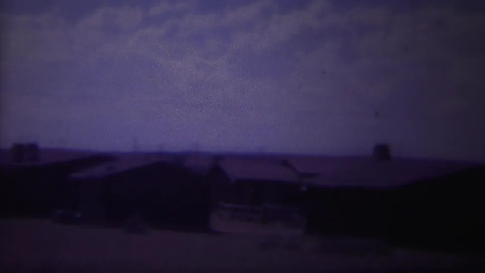 1967 8mm frame from Yellowstone, Wyoming showing dark low buildings under a heavy purple-blue sky.