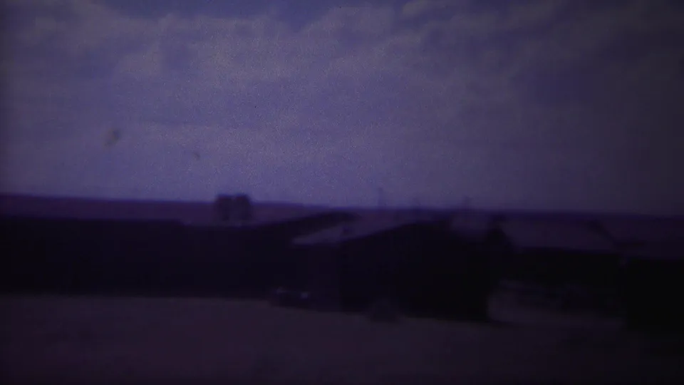 A soft 8mm view of low rural houses and dark rooflines beneath a purple, overcast Wyoming sky.